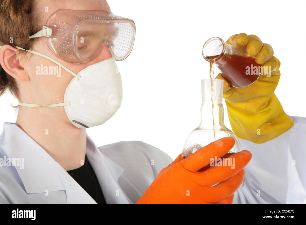 Vue sur scientifique au Respirateur et gants de caoutchouc liquide brun verse d'un ballon dans un autre Banque D'Images