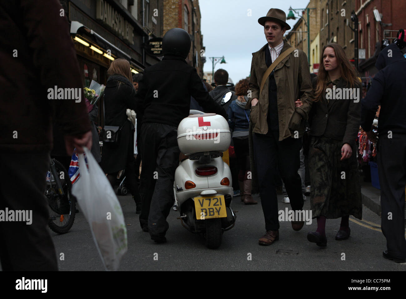 Un homme qui marche à travers la foule son scooter street dans l'East End londonien Banque D'Images