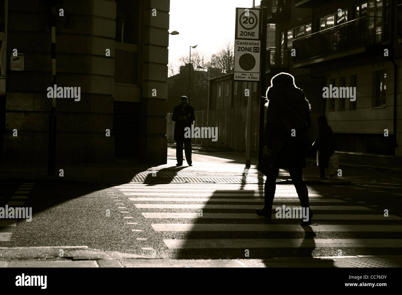 Une femme marche à travers un passage piétons à Londres et un homme se tient sur l'autre côté, photographié en sépia Banque D'Images