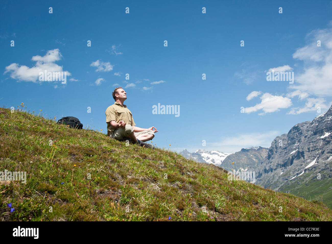 Homme assis sur le côté de la montagne, méditant, Oberland Bernois, Suisse Banque D'Images