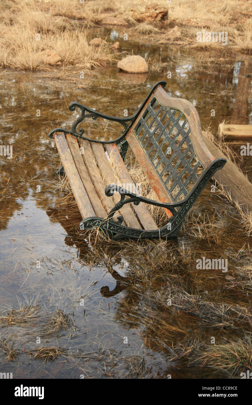 Un vieux bois et métal banc de parc s'enfonce dans une grande flaque Banque D'Images