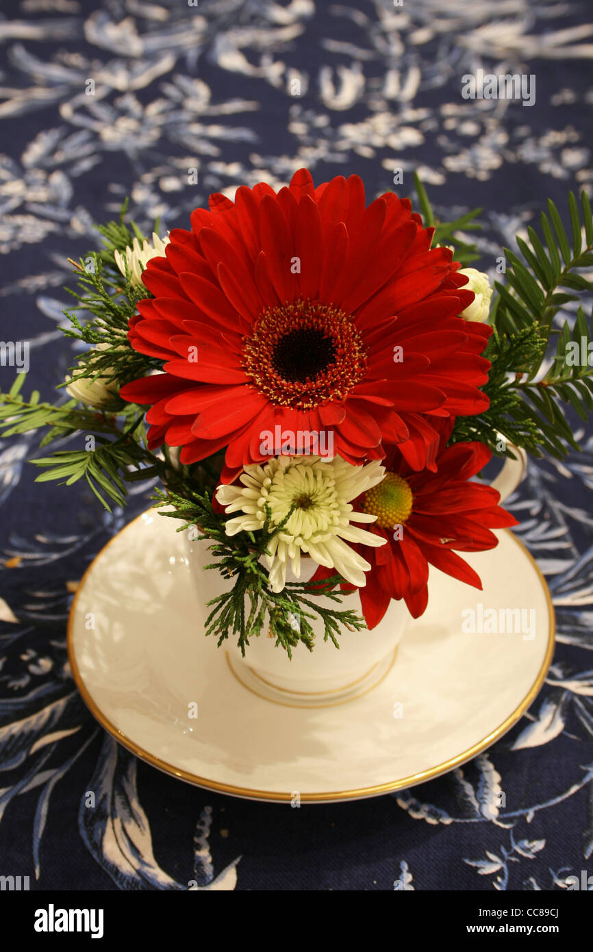 Vertical image de rouge et blanc fleurs dans une tasse comme une pièce maîtresse sur une nappe floral bleu Banque D'Images