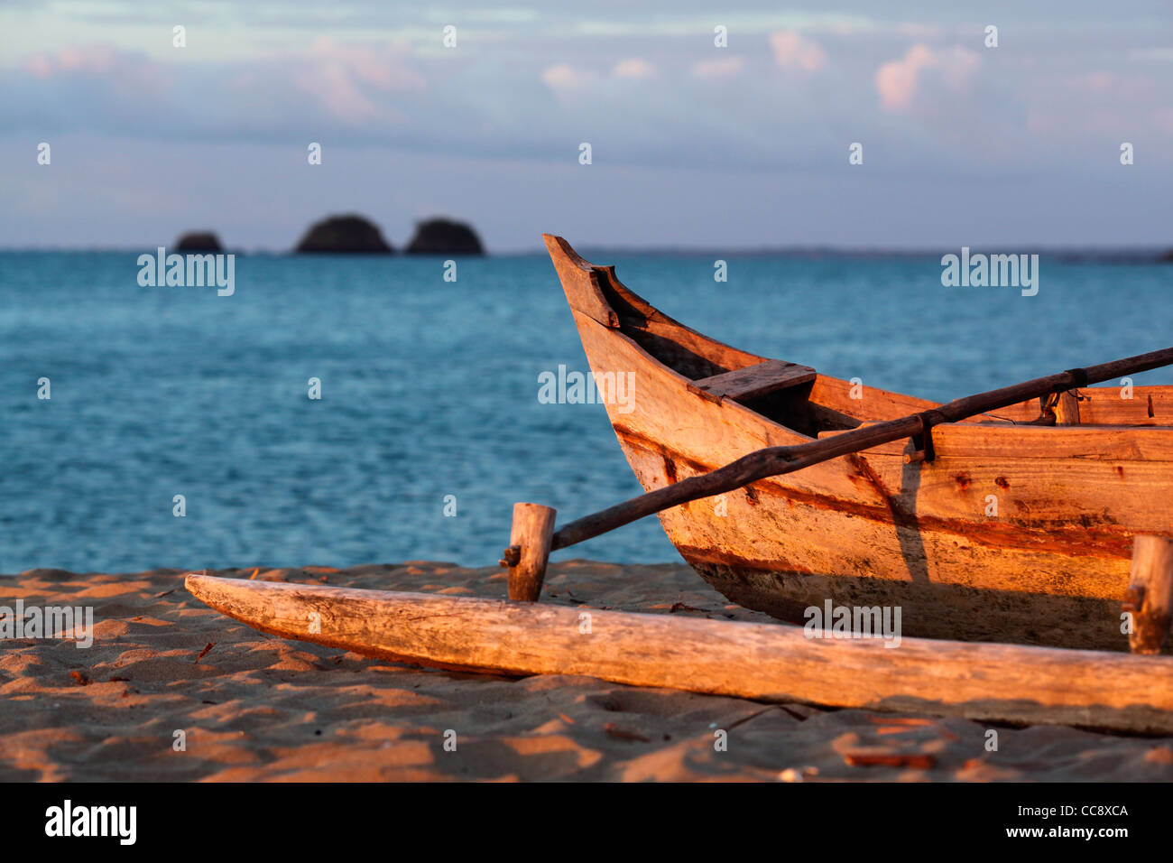 Échoués sur une pirogue à balancier, ou pirogue malgache, navire à voile, avec trois petites îles dans l'arrière-plan au coucher du soleil Banque D'Images