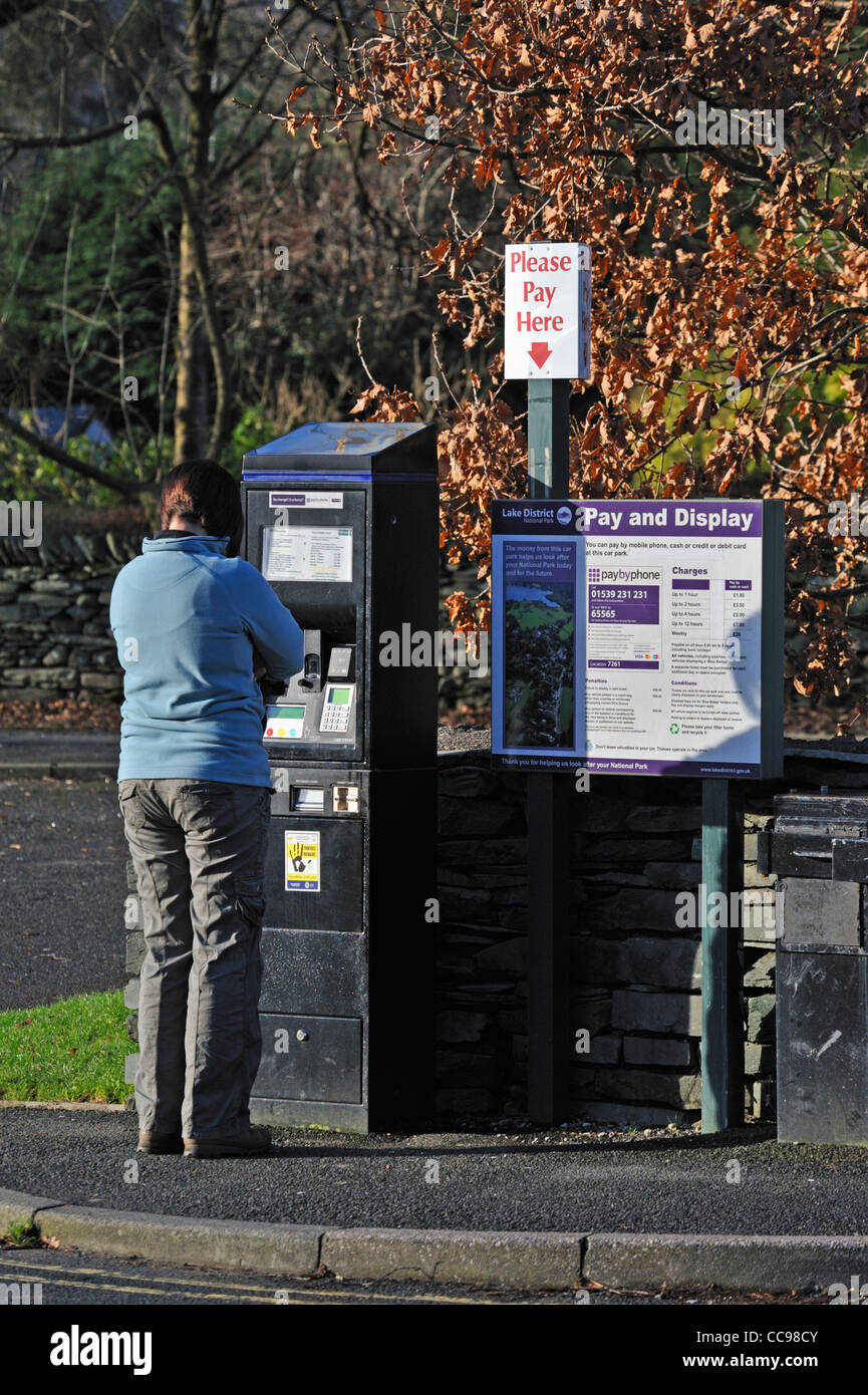 Femme à l'aide de payer et afficher un parcomètre. Grasmere, Parc National de Lake District, Cumbria, Angleterre, Royaume-Uni, Europe. Banque D'Images