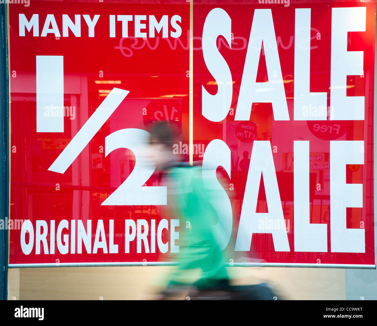 Une motion blurred personne marchant passé moitié prix vente affiches dans un shop store fenêtre, UK Banque D'Images