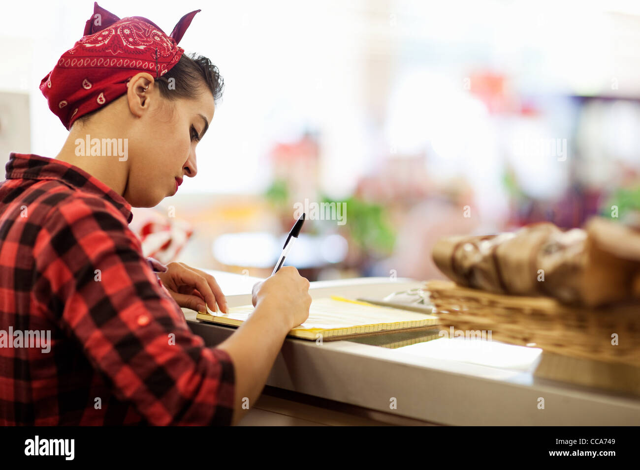 Jeune femme écrivant sur le comptoir de boulangerie Banque D'Images