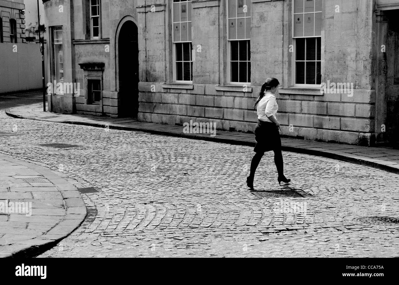 Une jeune femme qui traverse une rue pavée vide : Bath, Angleterre Royaume-uni Banque D'Images