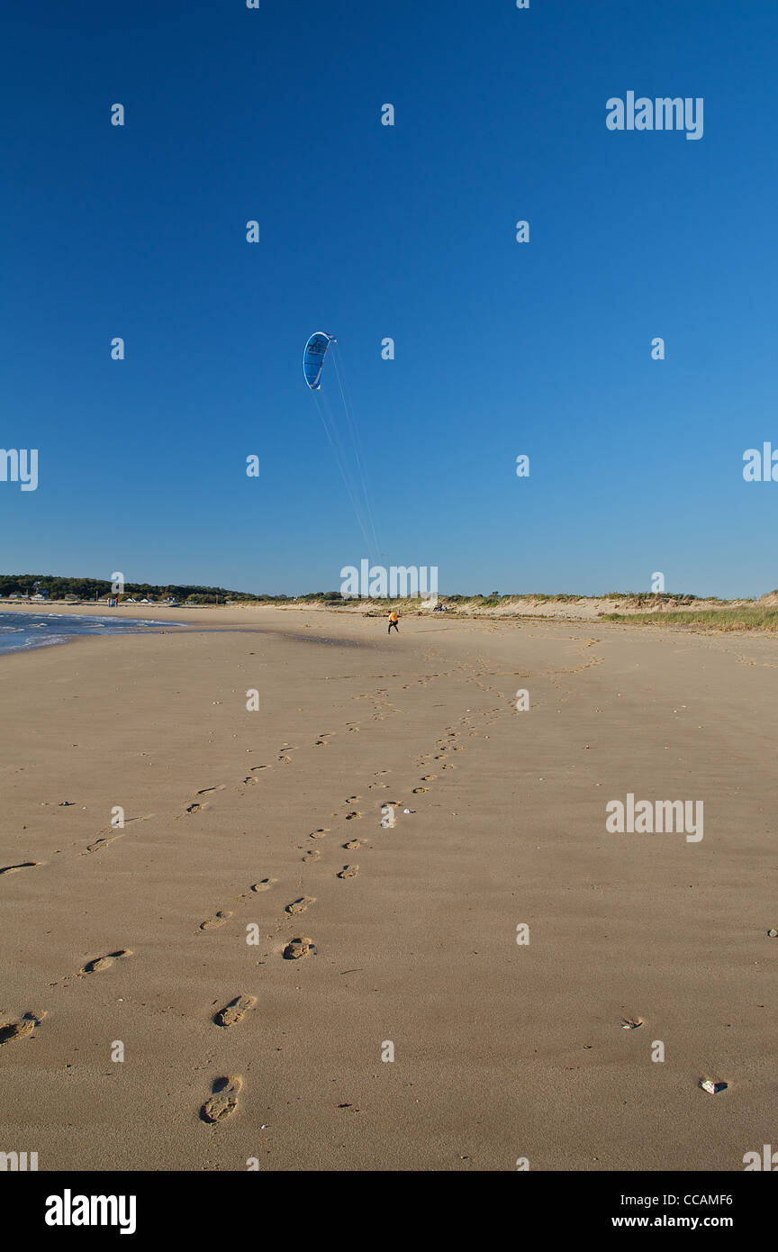 Des traces de pas dans le sable à marée basse menant à un kitesurfeur dans l'approche de l'eau distance Banque D'Images