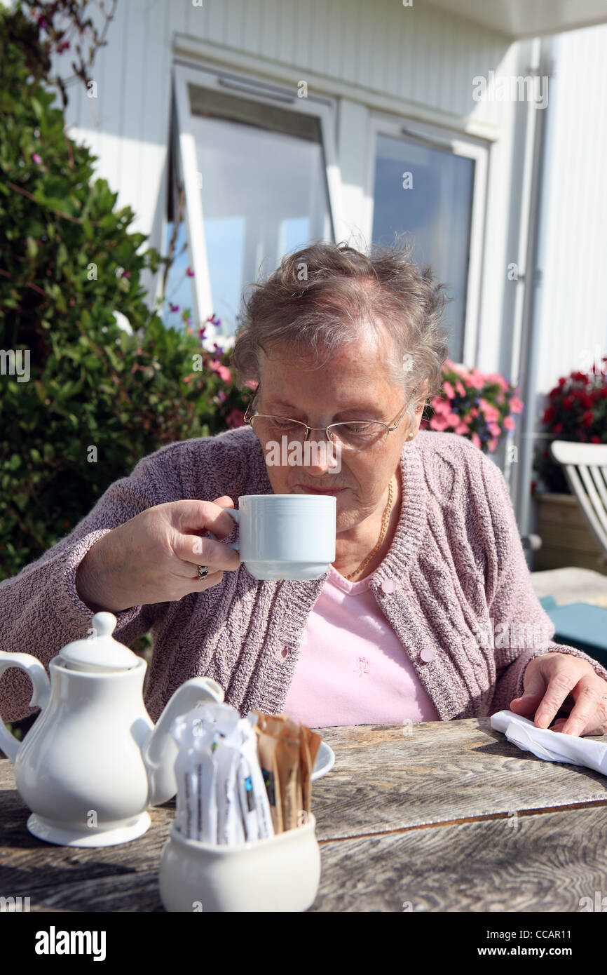Pensionné britannique bénéficiant de boire une tasse de thé à l'extérieur d'un restaurant en été Banque D'Images