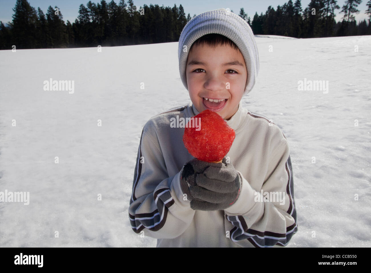 Garçon de 10 à 12 ans de manger un cône de neige à l'extérieur sur une journée d'hiver. Banque D'Images