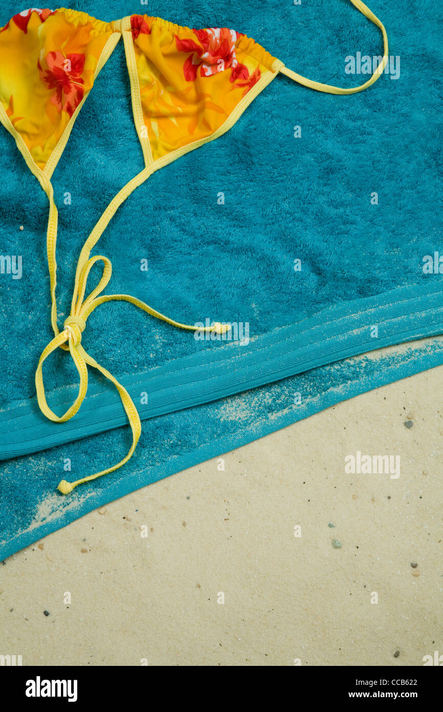Aqua Blue serviette sur le sable, les petits cailloux, shot, jaune, orange et rouge fleurs haut de bikini, jaune cordes tied in bow Banque D'Images