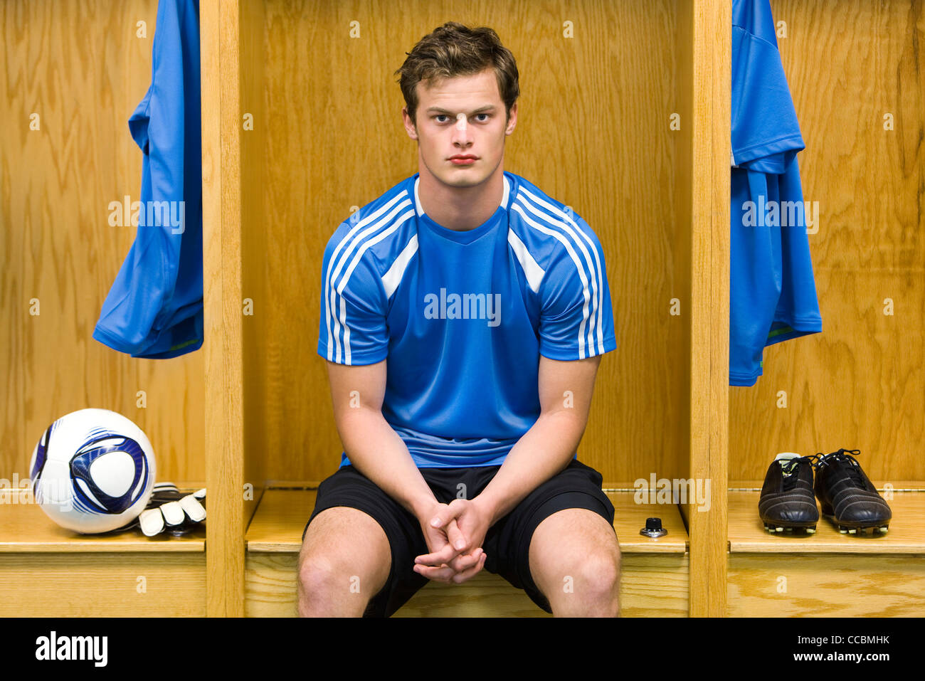 Jeune joueur de foot assis dans le vestiaire, portrait Banque D'Images