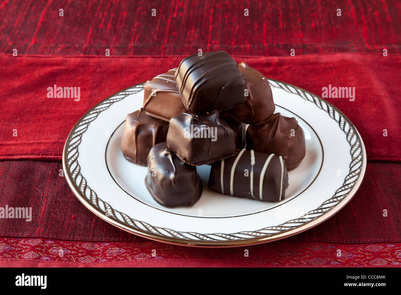 Chocolat au lait et noir bon-bons sur une fine plaque blanche de la chine avec de l'argent décoration sur la jante. Fond texturé rouge. Banque D'Images