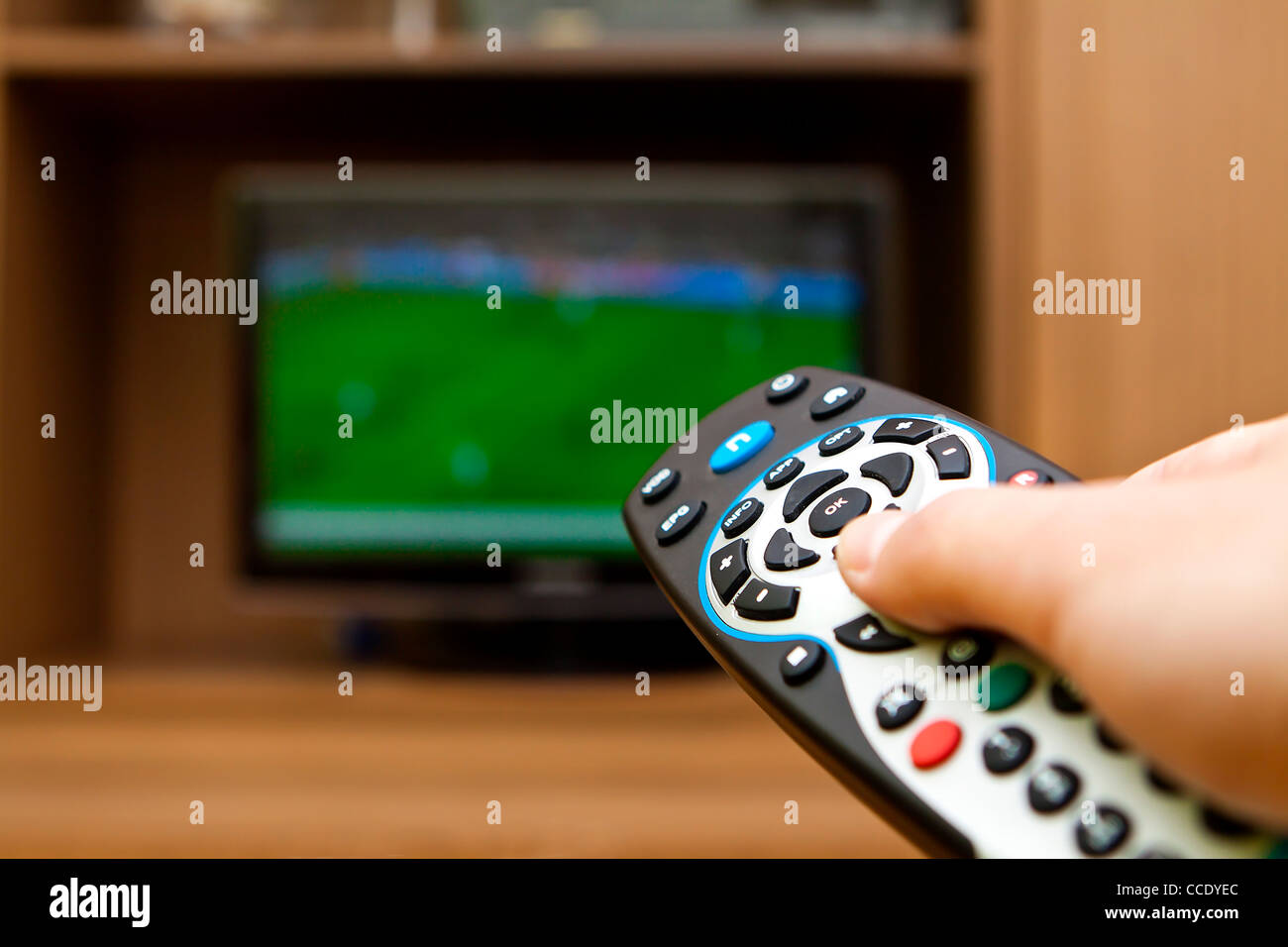 Main tenant la télécommande du téléviseur avec une télévision football. Banque D'Images
