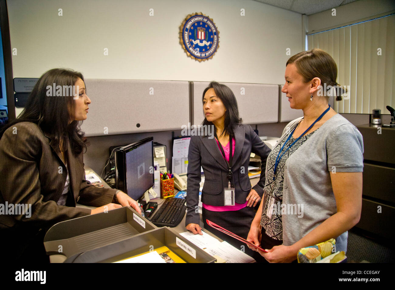 Les trois agents du FBI discuter d'un cas à Santa Ana, CA, bureau. Remarque Filipino-American en centre et logo fbi sur mur. Publié Banque D'Images