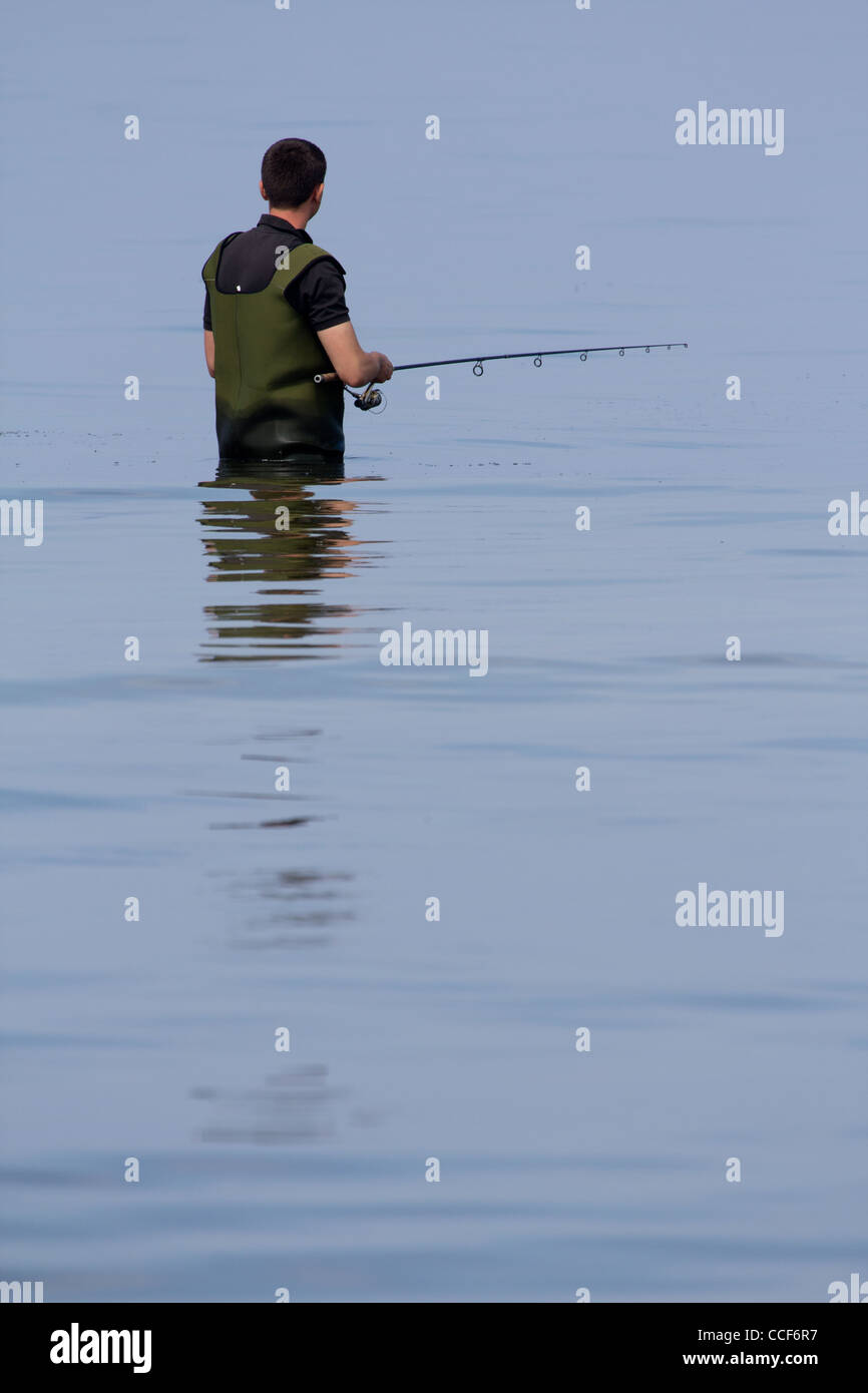 Un homme debout dans l'eau (mer Baltique), portant des pantalons de pêche. Dans les mains tenant une canne à pêche. Banque D'Images