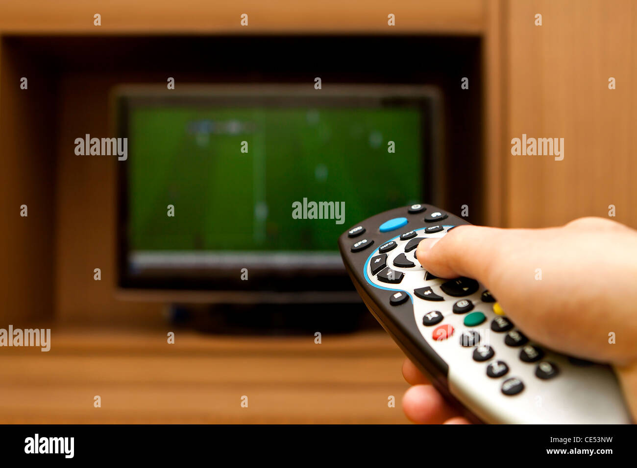 Main tenant la télécommande du téléviseur avec une télévision football. Banque D'Images