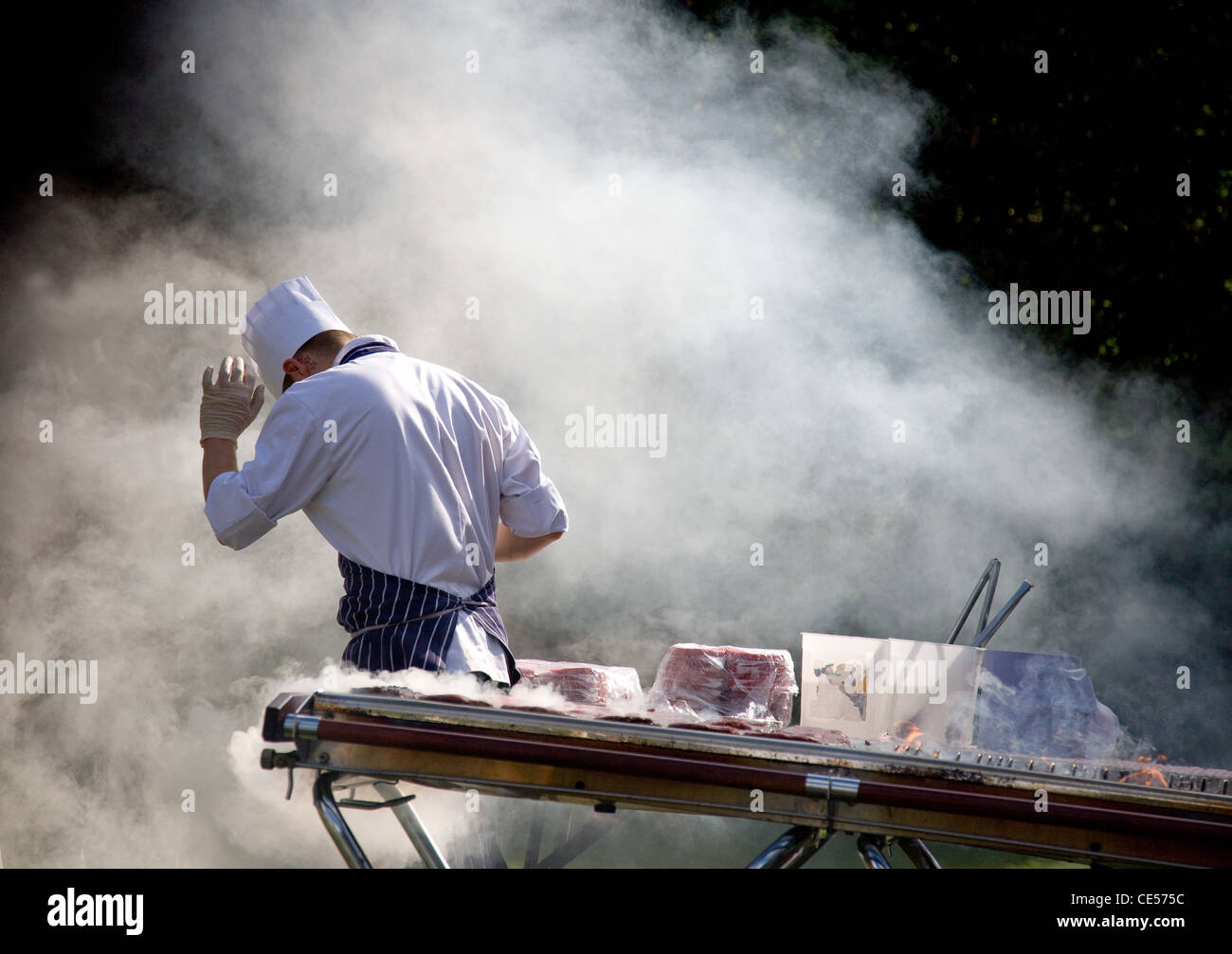 Un chef cuisiner des hamburgers at a garden party barbecue est submergé par la fumée de l'alimentation Banque D'Images