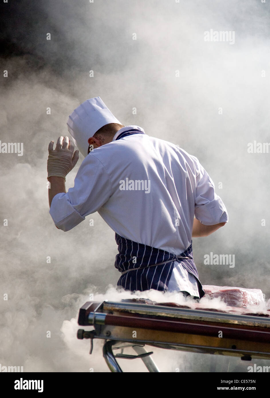 Un chef cuisiner des hamburgers at a garden party barbecue est submergé par la fumée de l'alimentation Banque D'Images