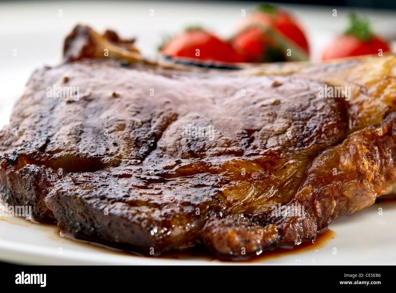 Steak Club. Sur l'os de veau. Macro de la viande grillée côtes sur plaque blanche avec des tomates cerises et dark hot sauce Banque D'Images