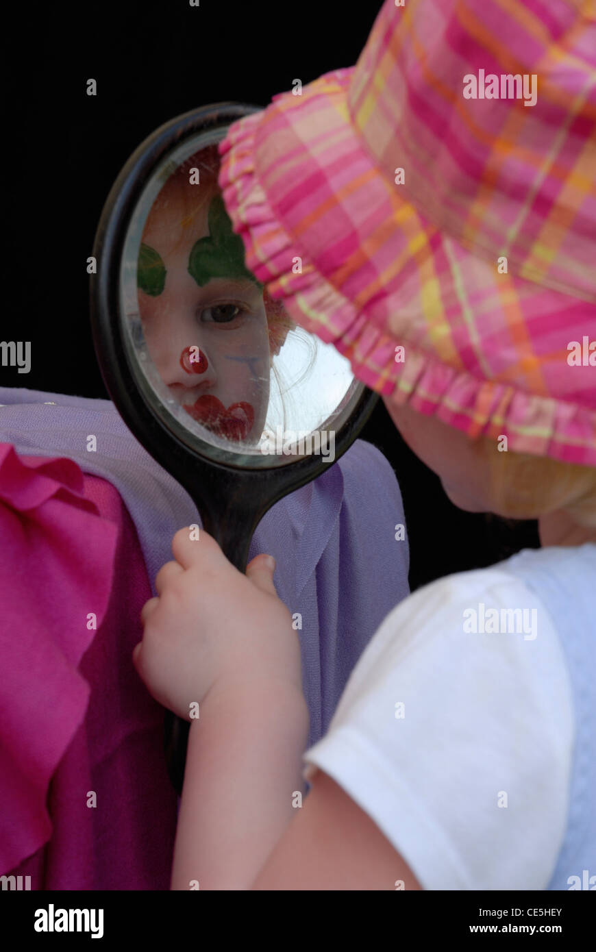 Petite fille avec la peinture pour le visage à la recherche d'un miroir d'elle-même Banque D'Images