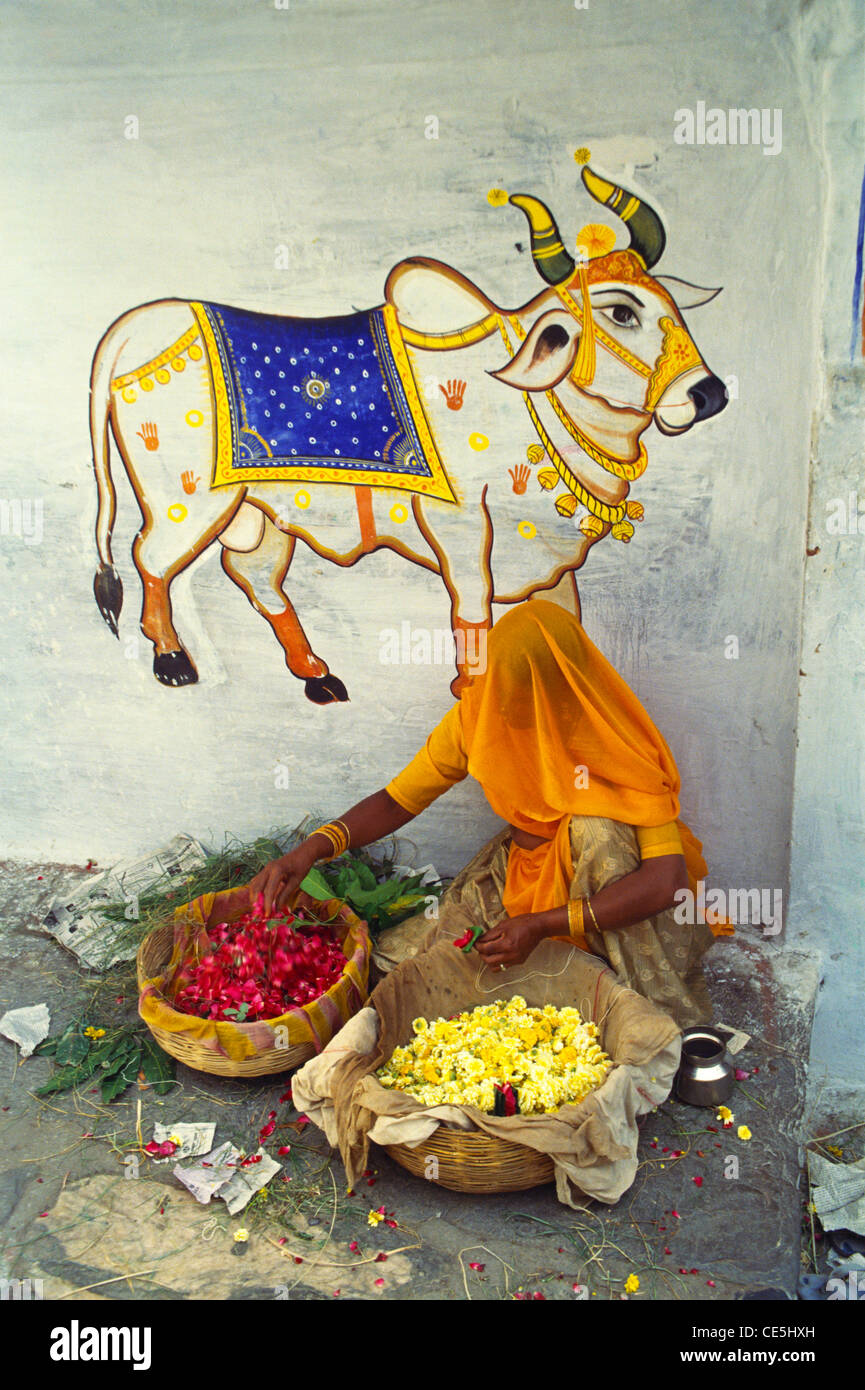 Femme vendeuse de fleurs en voile assis au-dessous de la peinture murale de vache ; ; ; Inde Rajasthan Jaipur Banque D'Images