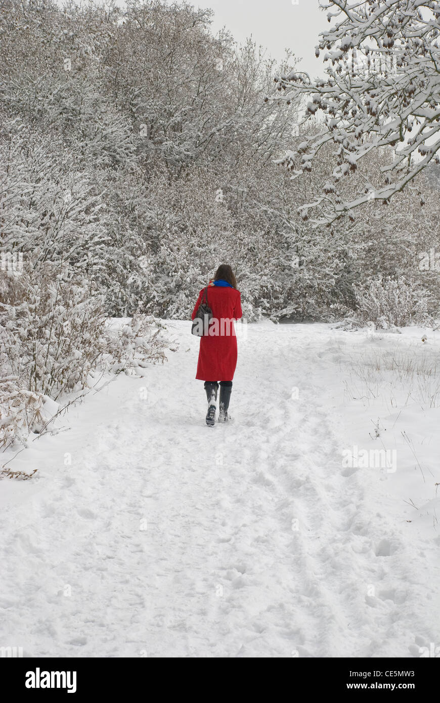 Girl in red coat walking in snow in park Banque D'Images