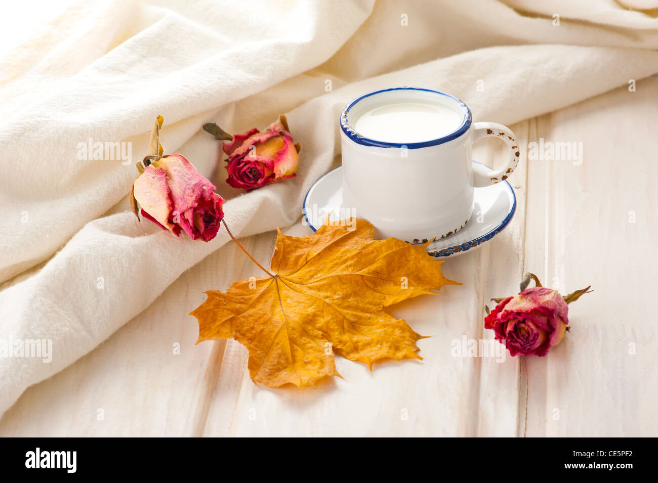 Le petit-déjeuner avec du lait. Dans le lait, tasse vintage roses sèches et de la feuille d'érable sur la vieille table en bois avec lin Banque D'Images