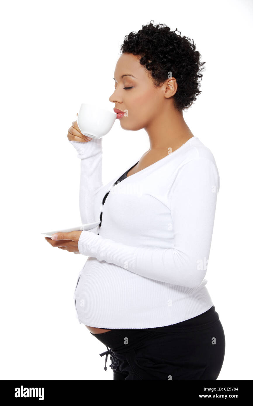 Vue du site portrait d'une belle femme enceinte tenant une tasse de café près de ses lèvres, isolé sur un fond blanc. Banque D'Images