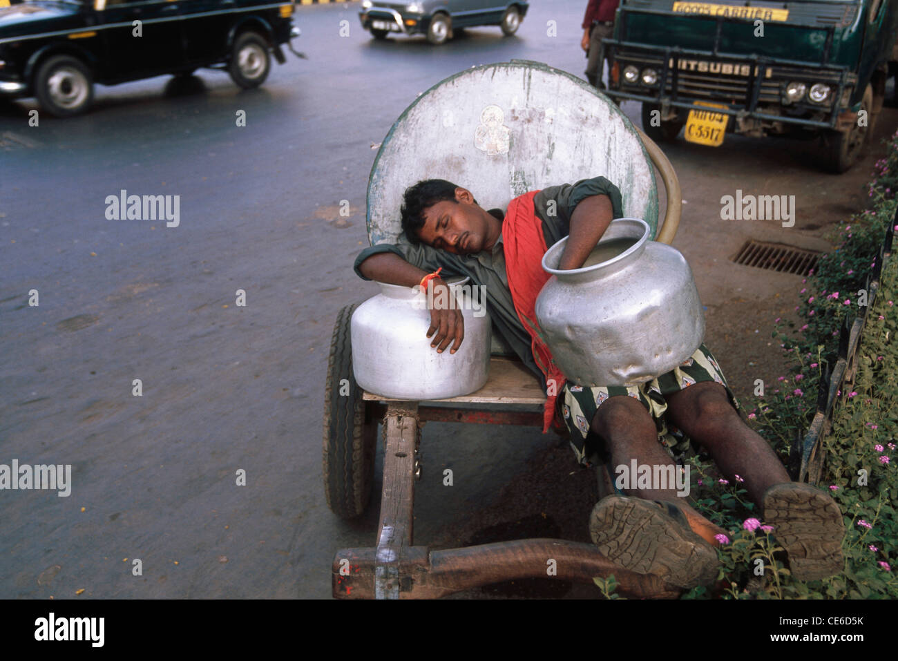 Man sleeping sur l'eau panier avec des marmites d'aluminium et de trafic Mumbai Inde Banque D'Images