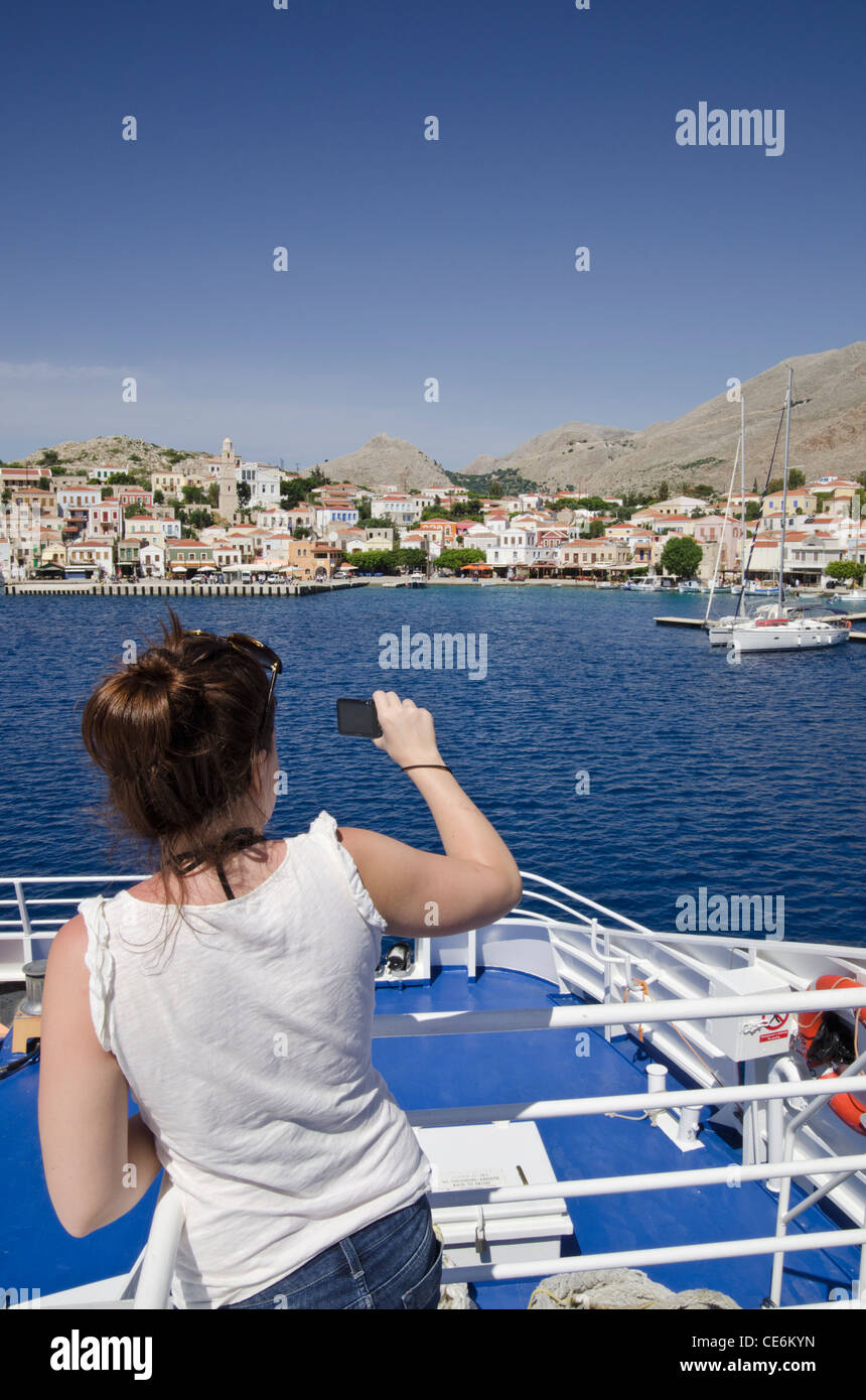 Femme de prendre une photo depuis le pont d'un traversier de l'île grecque, à l'approche du port d'Emborios dans l'île de Halki, Grèce Banque D'Images