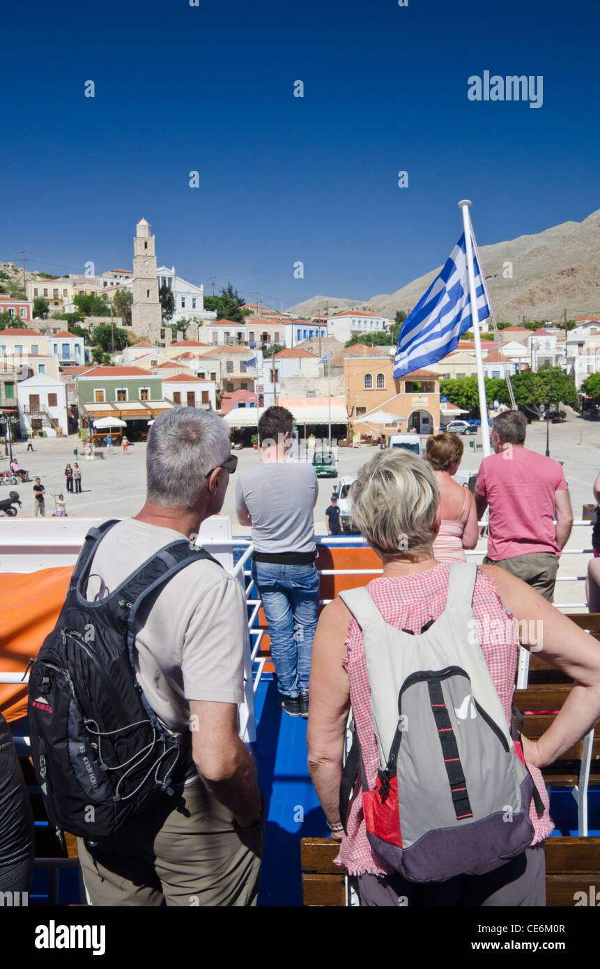 Les voyageurs profitant de la vue depuis le pont d'un ferry à mesure qu'il arrive dans la ville portuaire de l'île de Halki Emborios, Grèce Banque D'Images