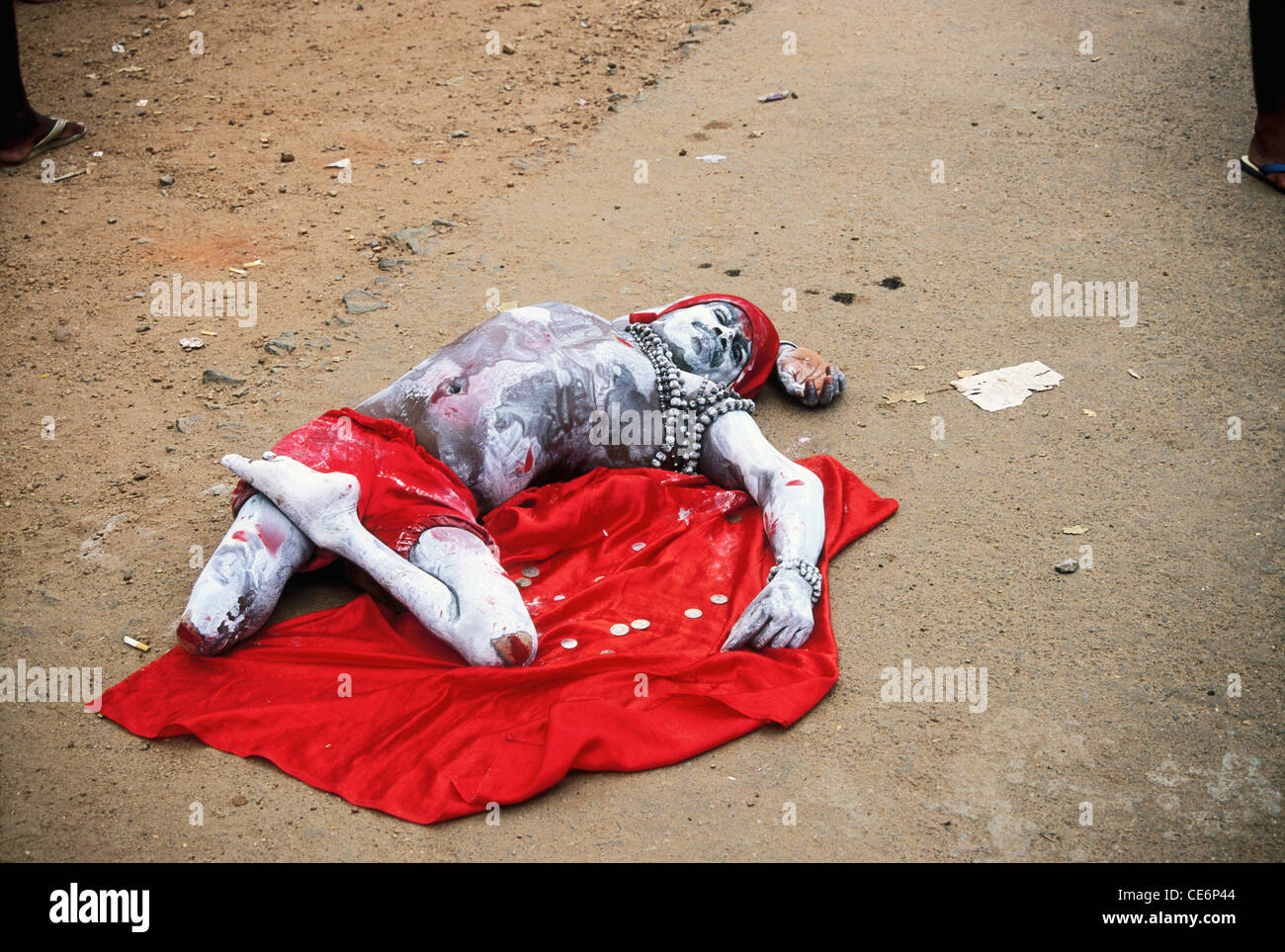 Mendiant avec jambe amputée frêne rouge couverts de tissu longe harnais rouge couché sur du tissu rouge et la mendicité ; Inde ; Kerala Banque D'Images