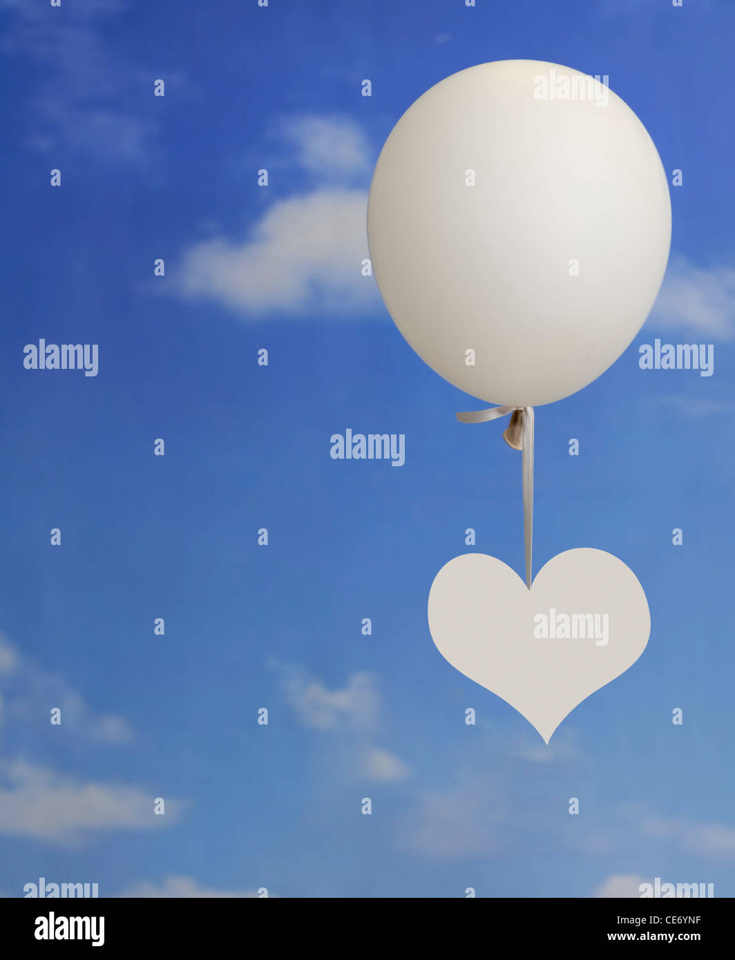 Forme de coeur blanc accroché à un ballon blanc contre un ciel bleu avec des nuages Banque D'Images