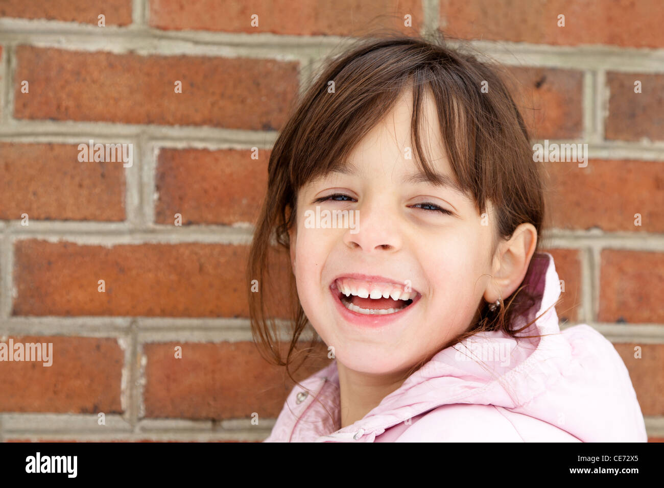 Rire petite fille en manteau d'hiver en face d'un mur de briques Banque D'Images