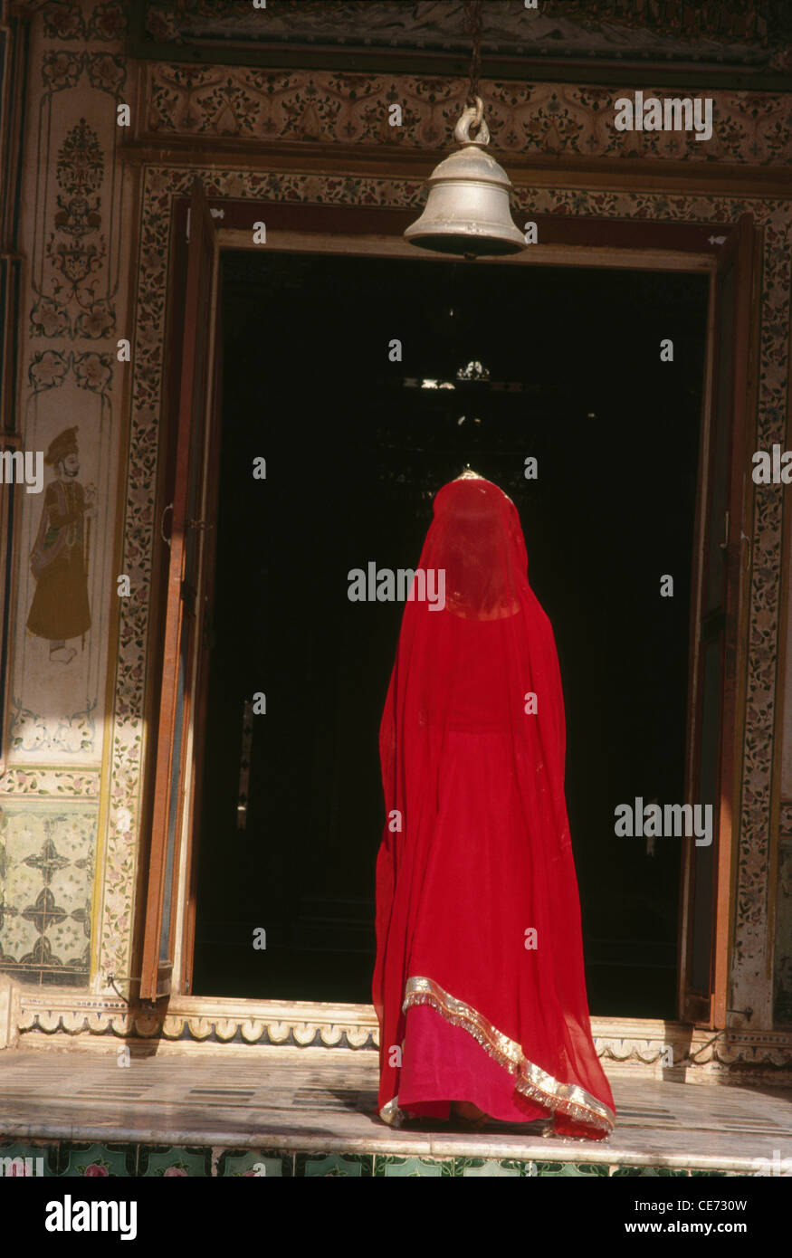 SHI 81815 : femmes indiennes en sari rouge priant ci-dessous cloche du temple le Rajasthan en Inde Banque D'Images