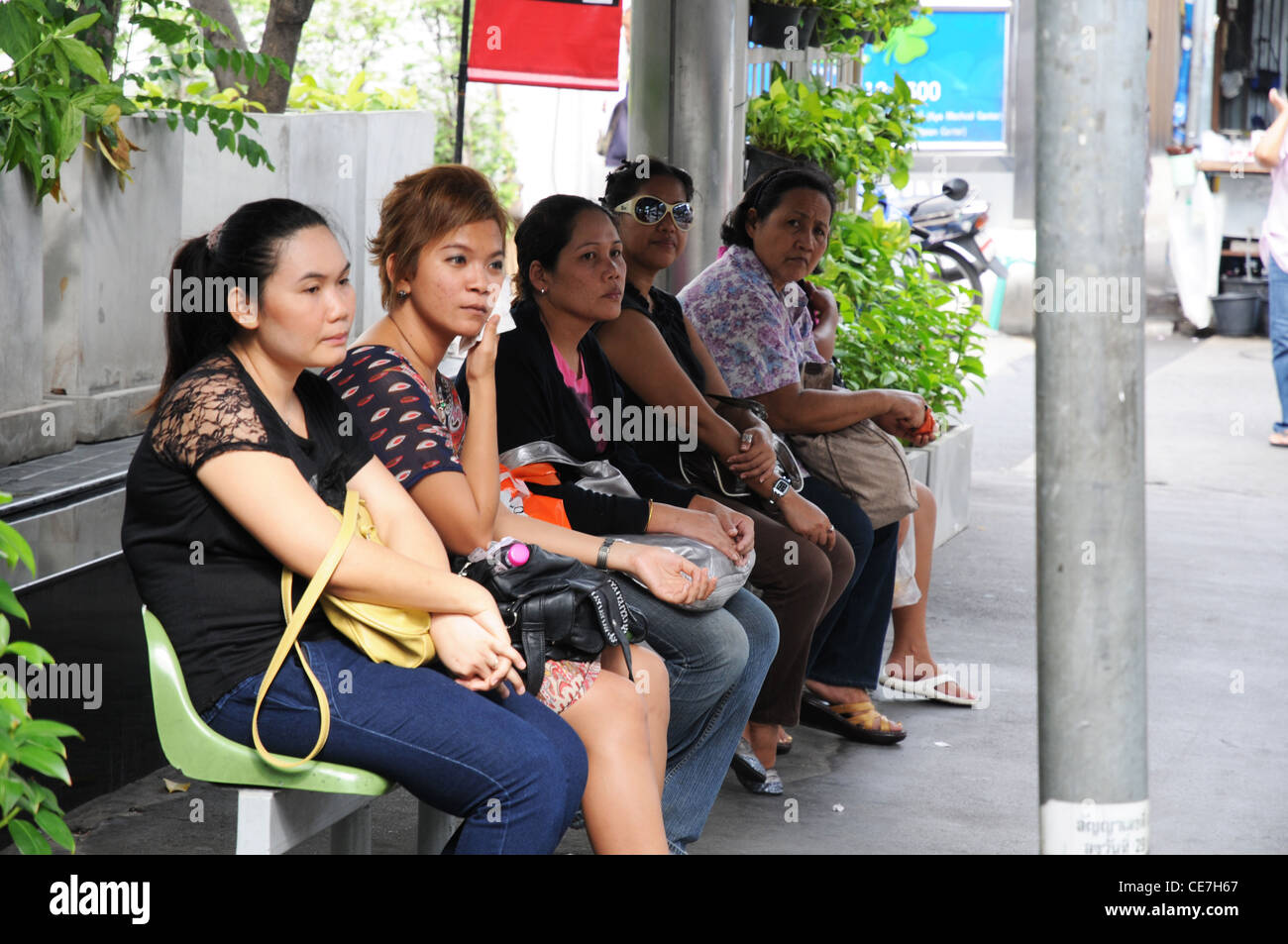 Les banlieusards, les gens, les femmes, les filles, s'asseoir à l'arrêt de bus, Sukhumvit Road, Bangkok, Thaïlande Banque D'Images