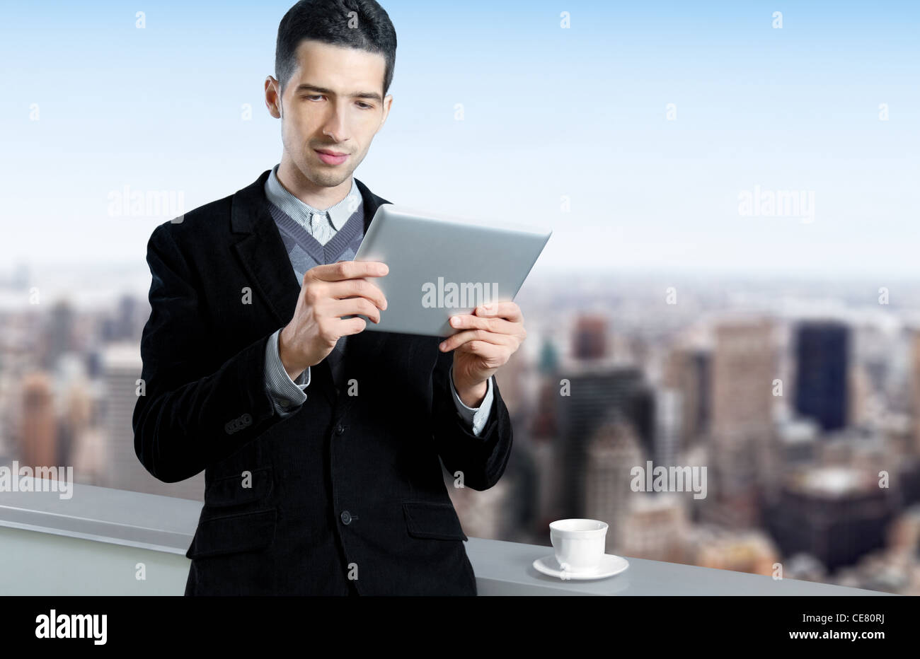 Jeune homme avec une tasse de café utilise une tablette numérique sur le toit d'un centre d'affaires. Cityscape floue avec des gratte-ciel Banque D'Images