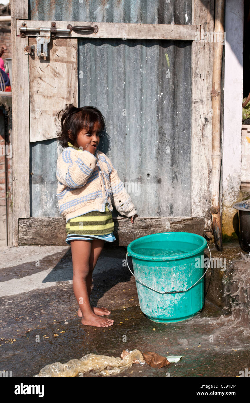 Petite fille à côté d'un seau d'eau en face de sa maison, Rishikesh, Inde Uttarakhand Banque D'Images