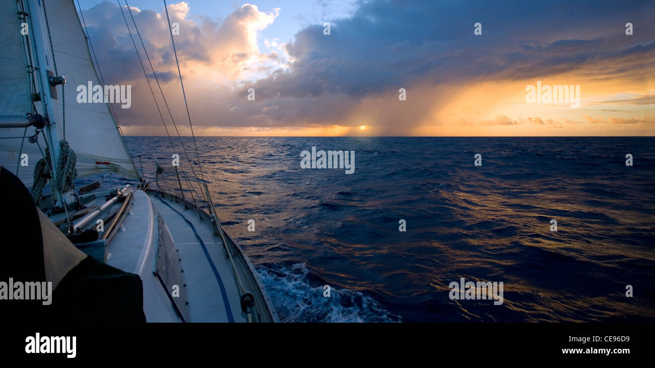 Un voilier sur un passage de l'océan se dirige vers le soleil et d'une petite bourrasque de pluie. Banque D'Images