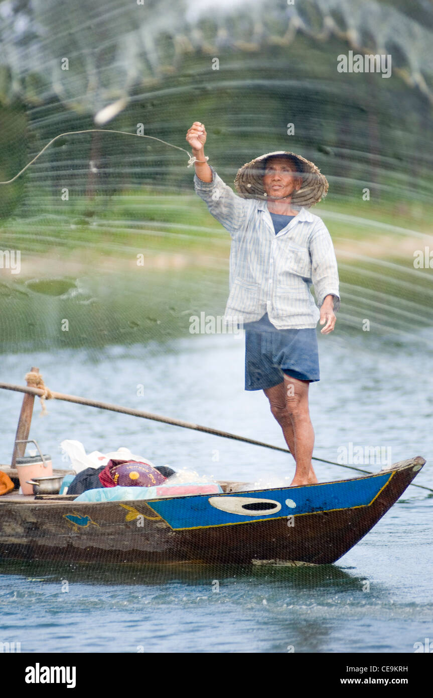 Un pêcheur balançoires son grand net pondéré sa tête ronde et dans les eaux de la rivière Thu Bon près de Hoi An au Vietnam. Banque D'Images