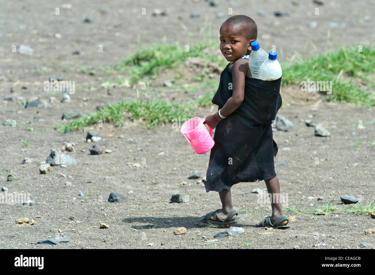 Enfant masaï transportant des bouteilles en plastique et une tasse dans Engaresero au lac Natron en Tanzanie Banque D'Images