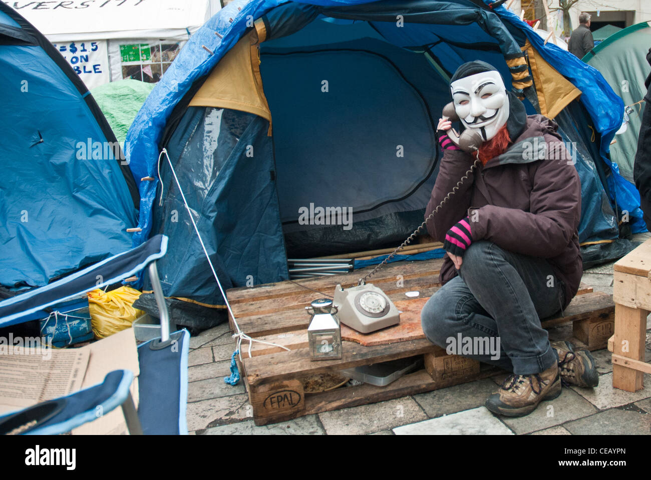 Occupy London, St Paul, "anonyme" assis en face de militants tente avec Guy Fawkes mask holding vieux téléphone. Banque D'Images