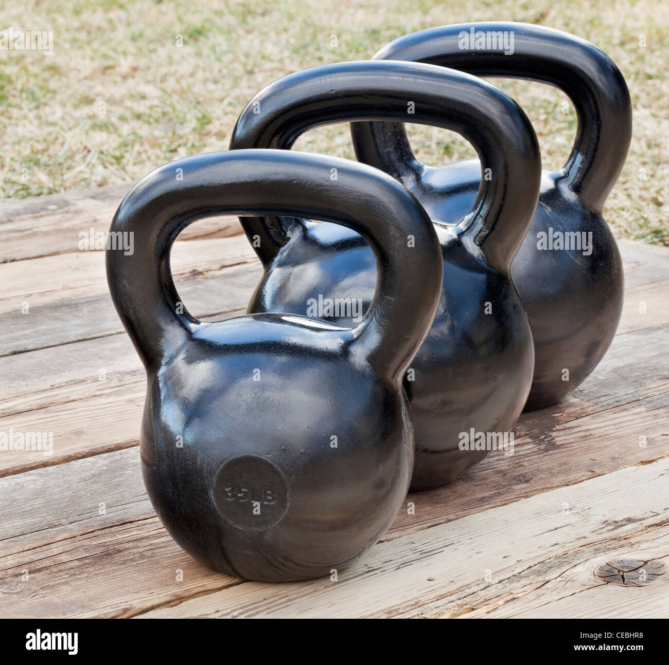 Trois kettlebell fer noir pour la formation de poids (35 et 50 lb) sur le pont de bois, en plein air avec des groupes grunge réflexions ciel Banque D'Images