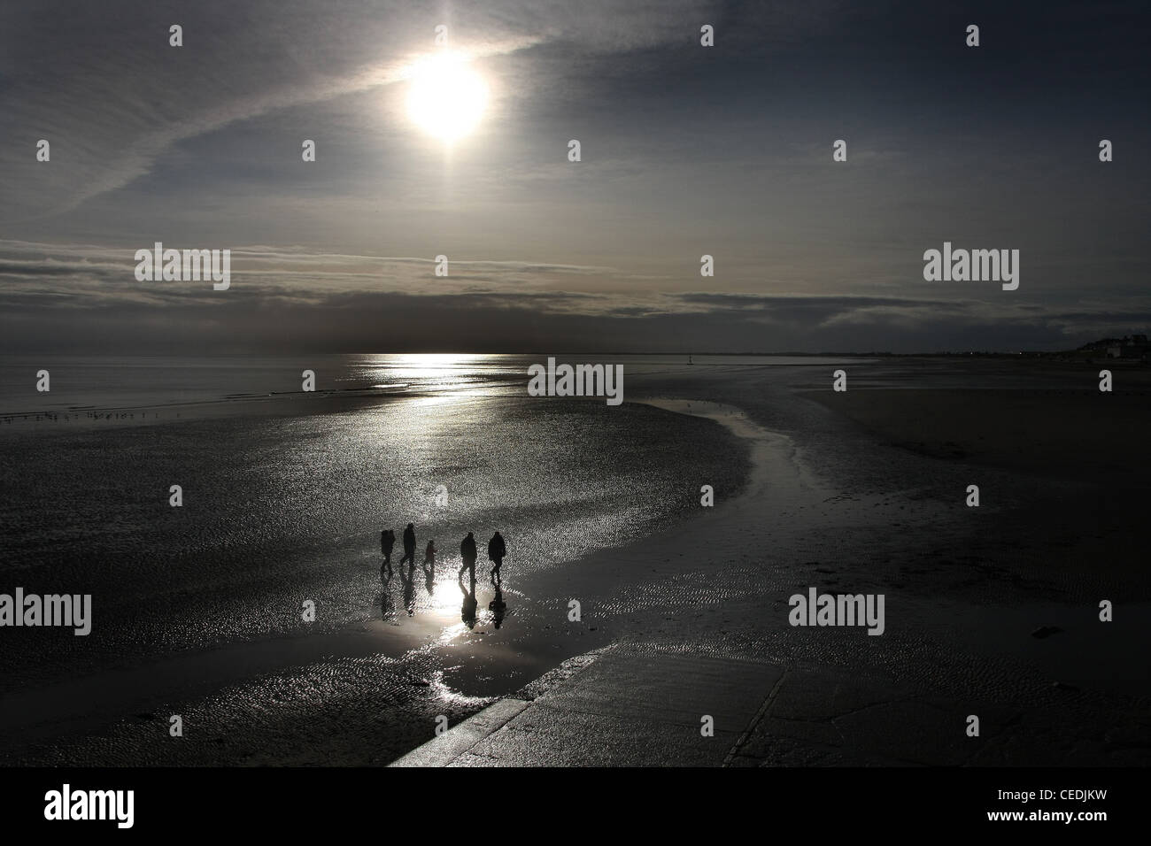 La silhouette d'une image de personnes marchant sur une plage à marée basse en plein soleil du matin. Banque D'Images