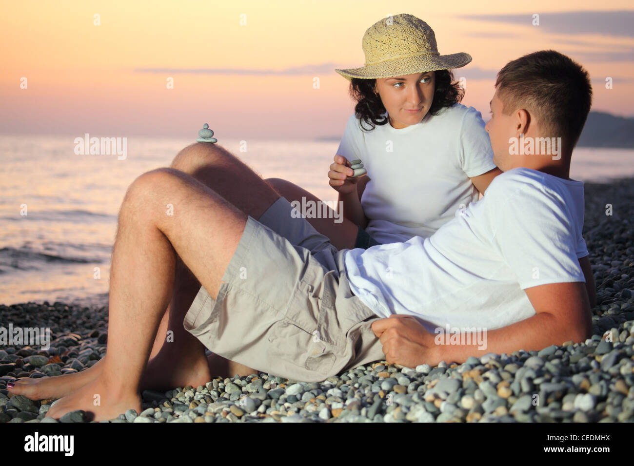 Jeune homme et femme en chapeau de paille pyramides design du pebble sur Stony Beach en soir Banque D'Images