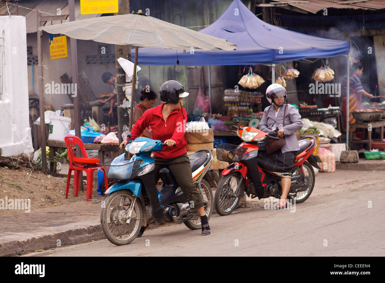 Deux femmes locales sur des cyclomoteurs à l'extérieur les étals du marché alimentaire de tôt le matin à Luang Prabang Banque D'Images