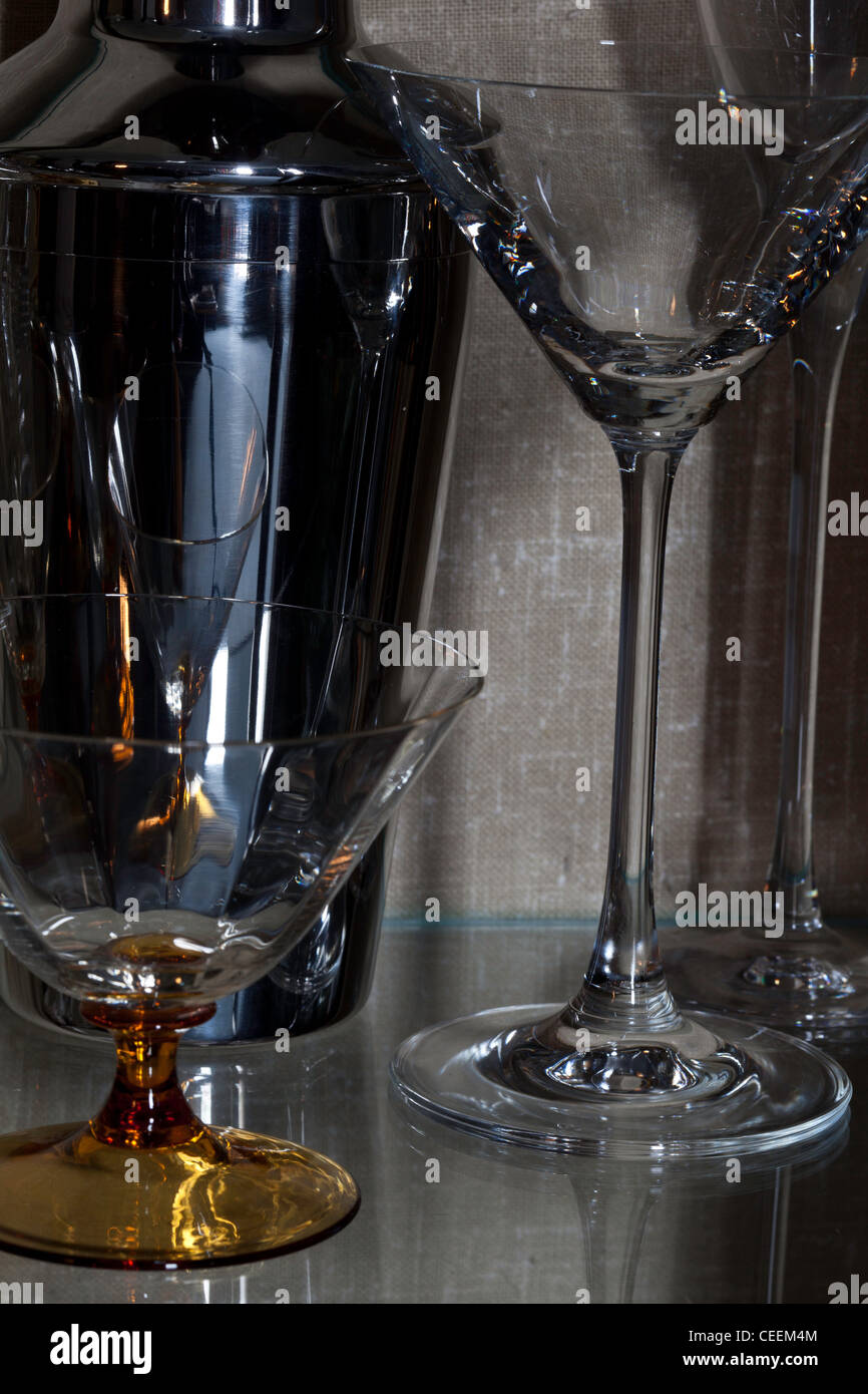 Chrome shaker et cocktail et verres de champagne sur une étagère en verre du cabinet. Banque D'Images