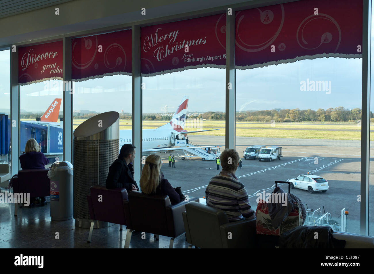 dh salon de départ SCOTTISH AIRPORT EDINBURGH SCOTLAND passagers regardant l'avion de ba piste vue intérieur People terminal Banque D'Images