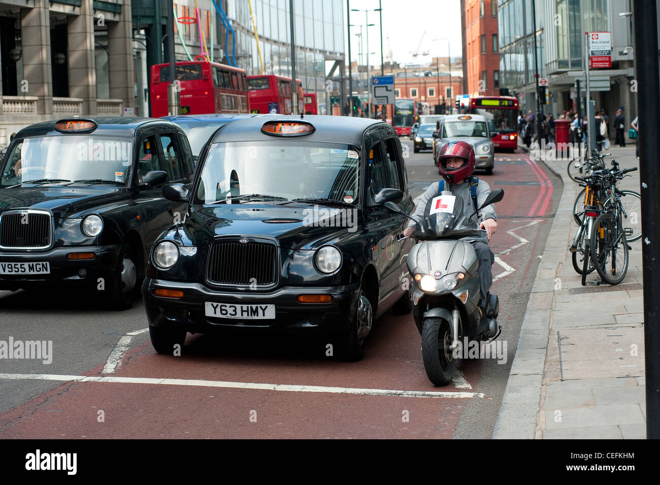 L'homme de la trottinette en attente à côté d'un taxi noir de Londres, le trafic de l'Angleterre. Banque D'Images
